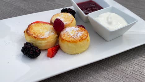 Delicious-syrniki-with-forest-berries,-sour-cream-and-jam,-breakfast-mini-cottage-cheese-pancakes,-traditional-ukrainian-russian-dish,-brunch-restaurant,-4K-shot