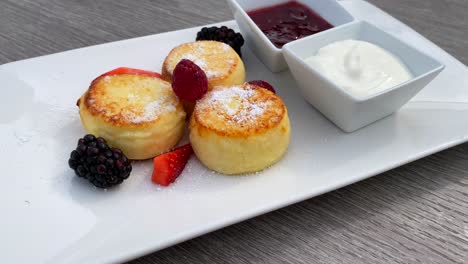 Köstliche-Syrniki-Mit-Waldbeeren,-Sauerrahm-Und-Marmelade,-Mini-Hüttenkäse-Pfannkuchen-Zum-Frühstück,-Traditionelles-Ukrainisches-Russisches-Gericht,-Brunch-Restaurant,-4K-Aufnahme