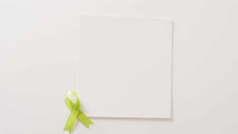 Video-of-pale-green-std-awareness-ribbon-and-white-card-with-copy-space,-on-white-background