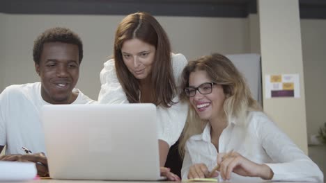 cheerful colleagues watching funny content on laptop