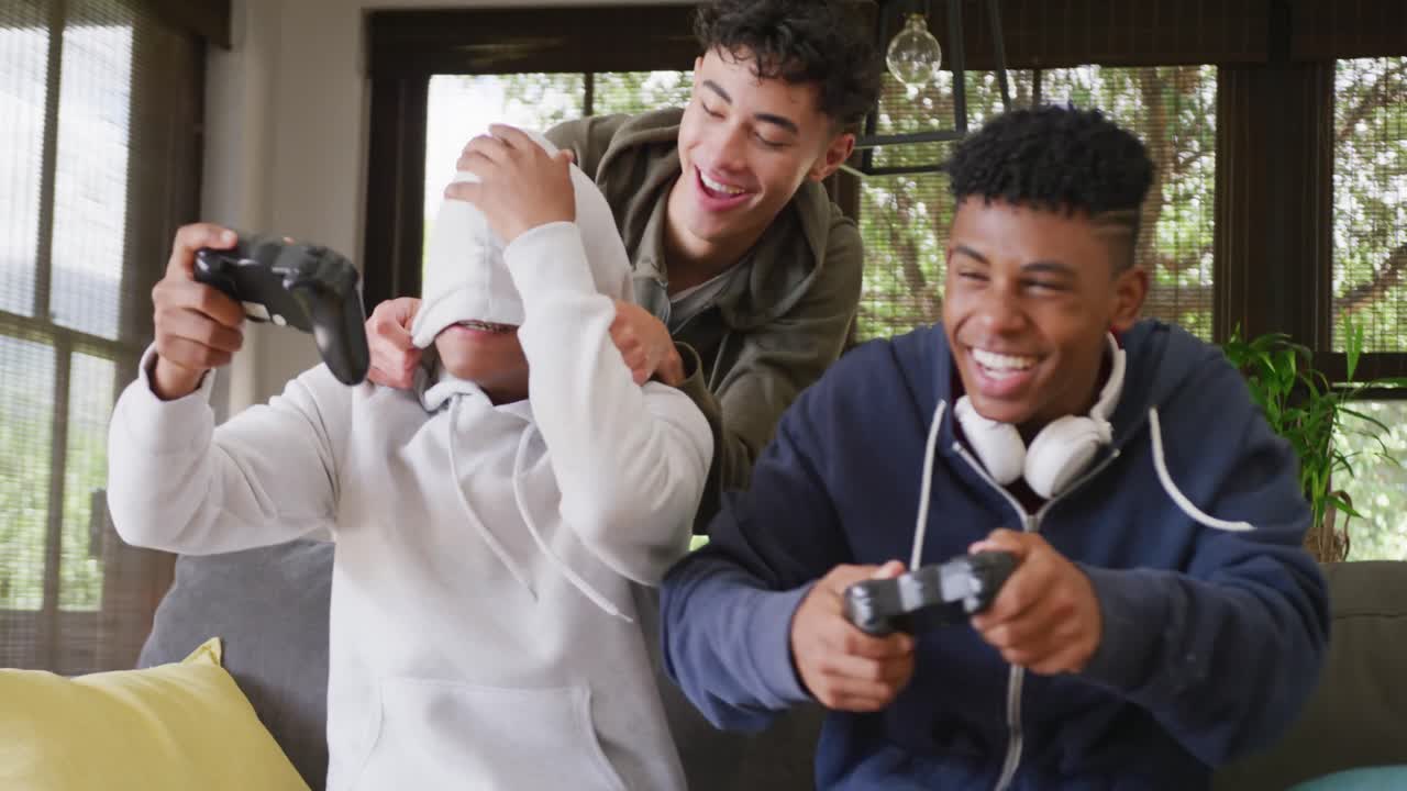 Happy diverse male teenage friends playing video games at home, slow motion