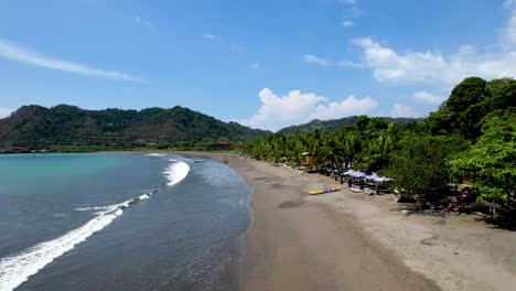 Costa-Rican-tropical-beach-with-boats,-palm-trees-and-small-waves