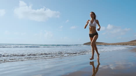 fitness runner woman running on beach listening to music motivation with phone case sport armband strap. sporty athlete training cardio barefoot with determination under summer sun.