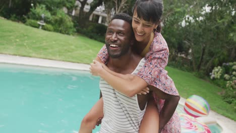 Happy-diverse-couple-at-swimming-pool,-man-carrying-woman-in-garden