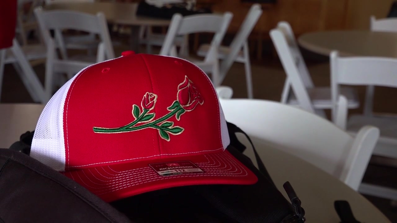 Close-up of a red baseball cap featuring a rose embroidery placed on a table indoors.