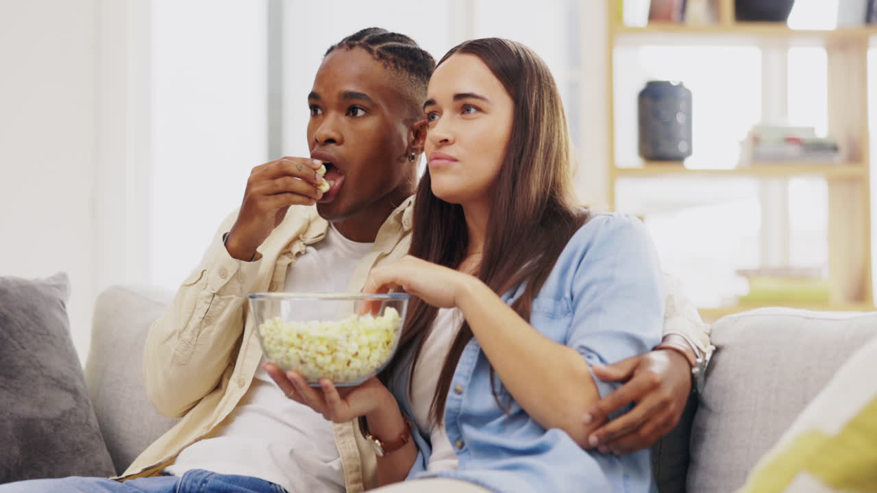 pareja, comiendo palomitas de maíz y viendo televisión en casa