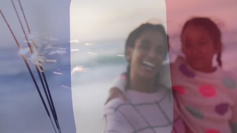 Animation-of-flag-of-france-over-biracial-mother-and-daughter-sitting-at-beach