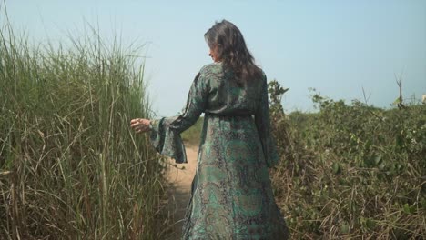 Cinematic-footage-of-girl-walking-towards-beach-playing-with-long-grass-on-her-way-past