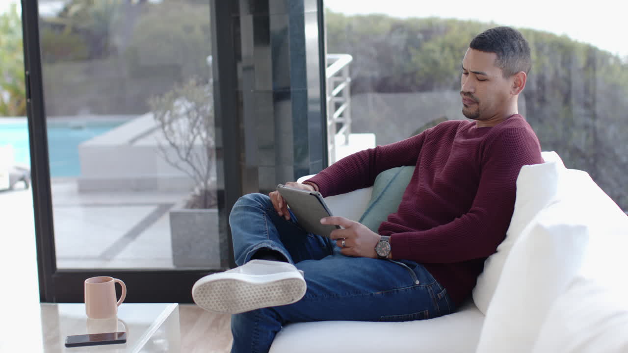 Using tablet, man sitting on couch in modern living room