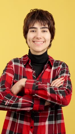 smiling young woman with short hair wearing a red plaid shirt and a black turtleneck against a yellow background