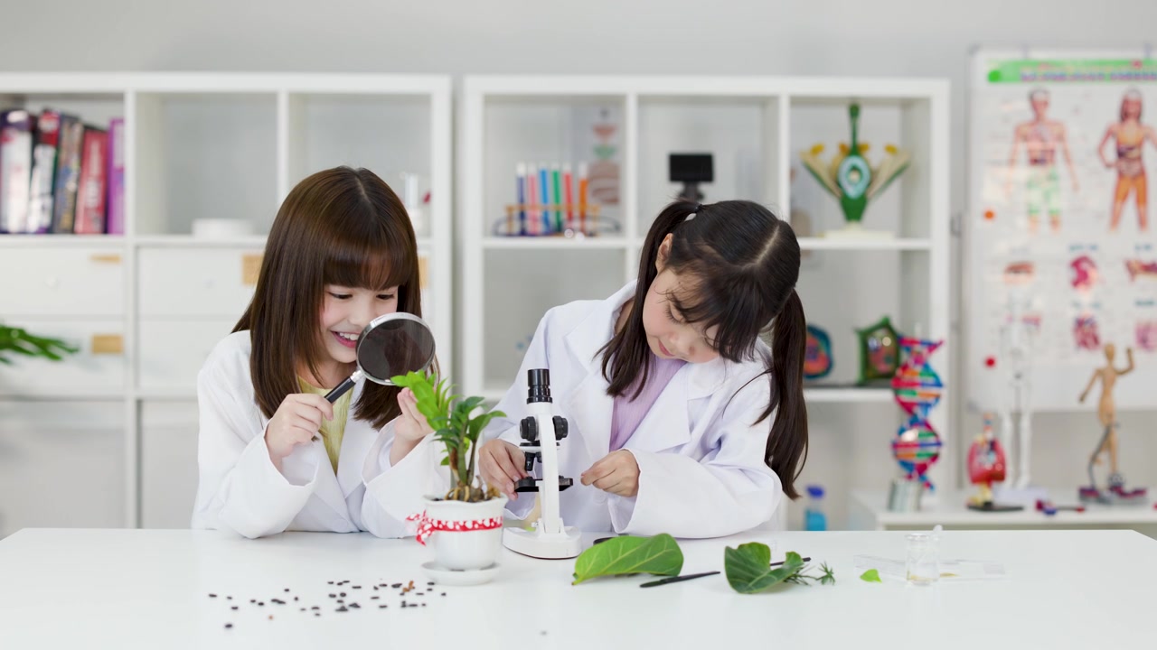 Two young Asian students examine plant specimens using a microscope and magnifying glass in school.
