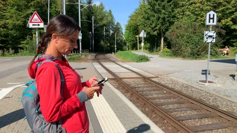 Sporty-older-woman-looking-at-her-phone-while-waiting-for-the-train-facing-the-train-tracks