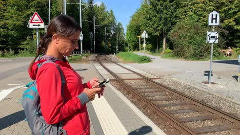 sporty older woman looking at her phone while waiting for the train facing the train tracks