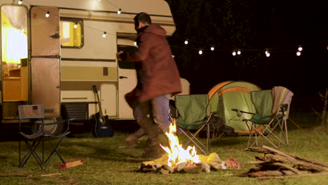 cheerful young couple dancing around camp fire in cold night of autumn