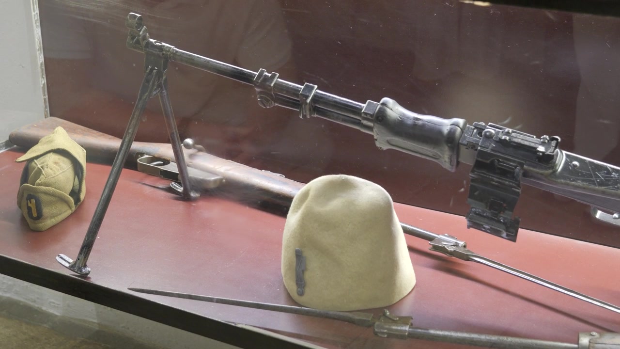 Exposição do Museu Bunk'Art 2 em Tirana, Albânia, com rifles, bipé, baioneta e gorro branco tradicional.