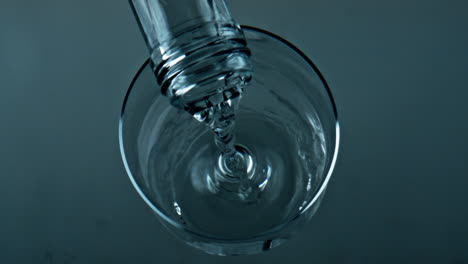 bottle pouring pure water into transparent cup closeup. top view liquid filling