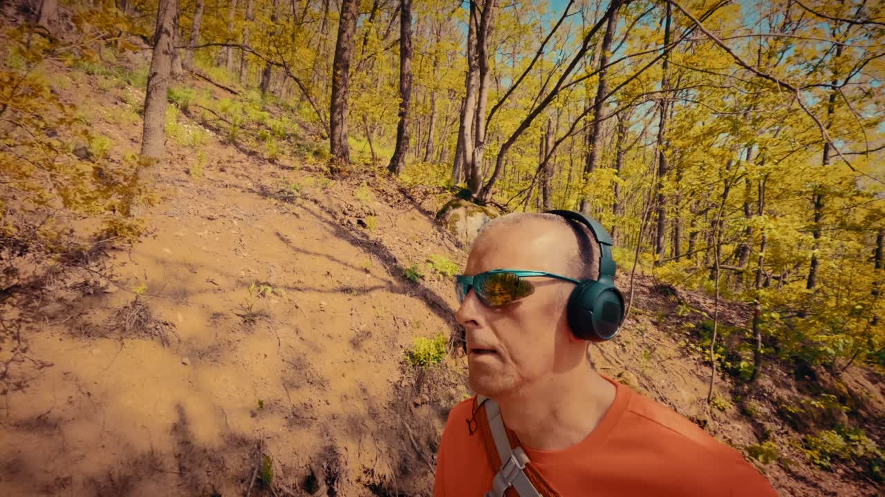 Un uomo maturo e rilassato sulla cinquantina ascolta musica in cuffia durante un'escursione. Concetto di sollievo per la salute mentale, riduzione dello stress e pace nella natura. Filmato 4K di alta qualità.