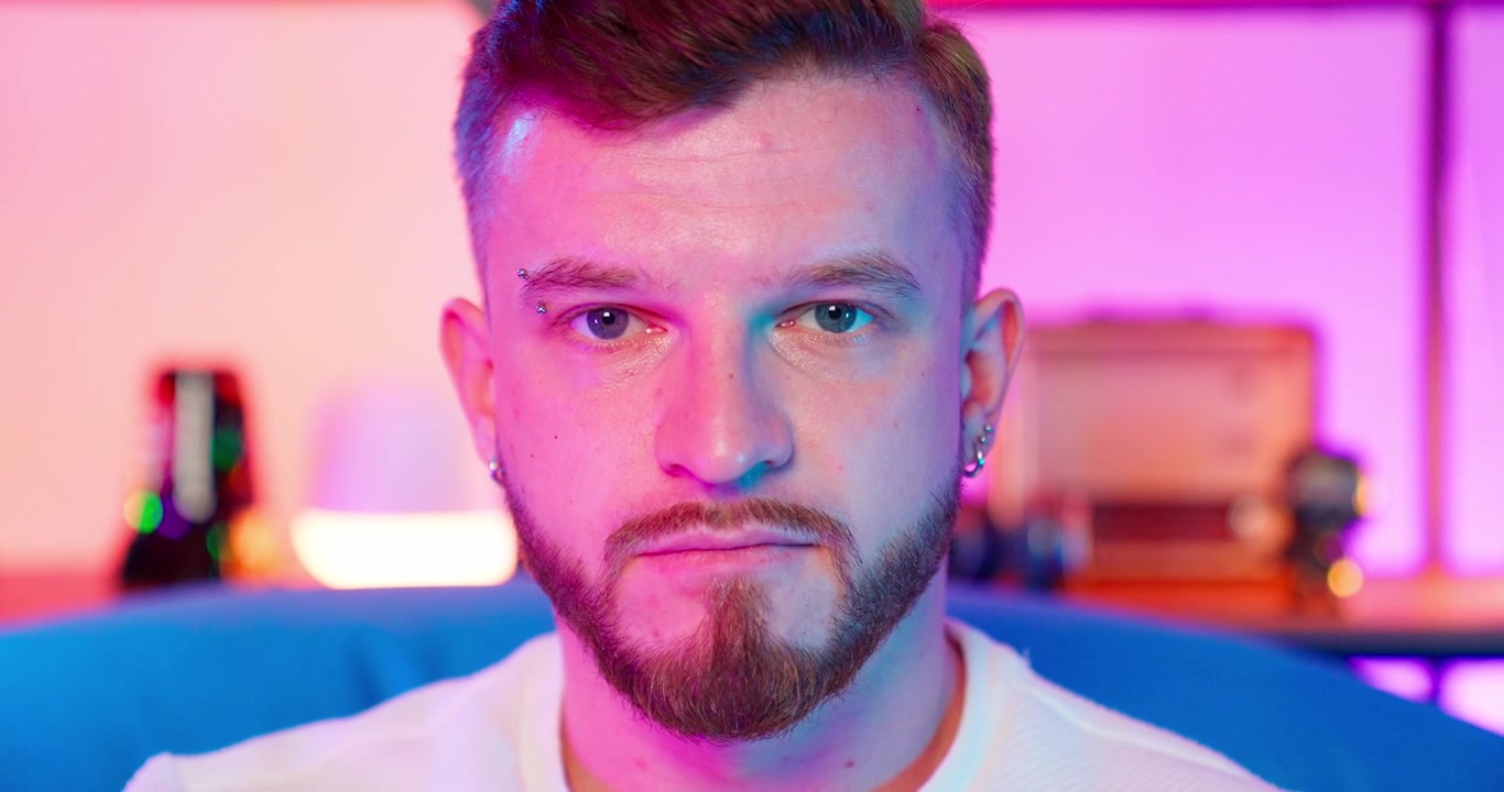 Ritratto ravvicinato di giovane uomo con barba e piercing sotto luce al neon