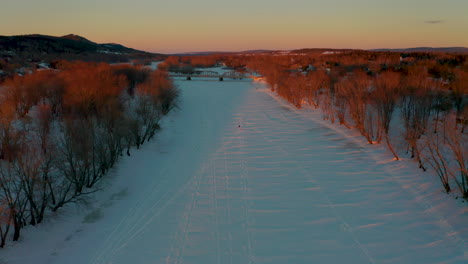 winter aerial view flying along a frozen snow covered river at sunset