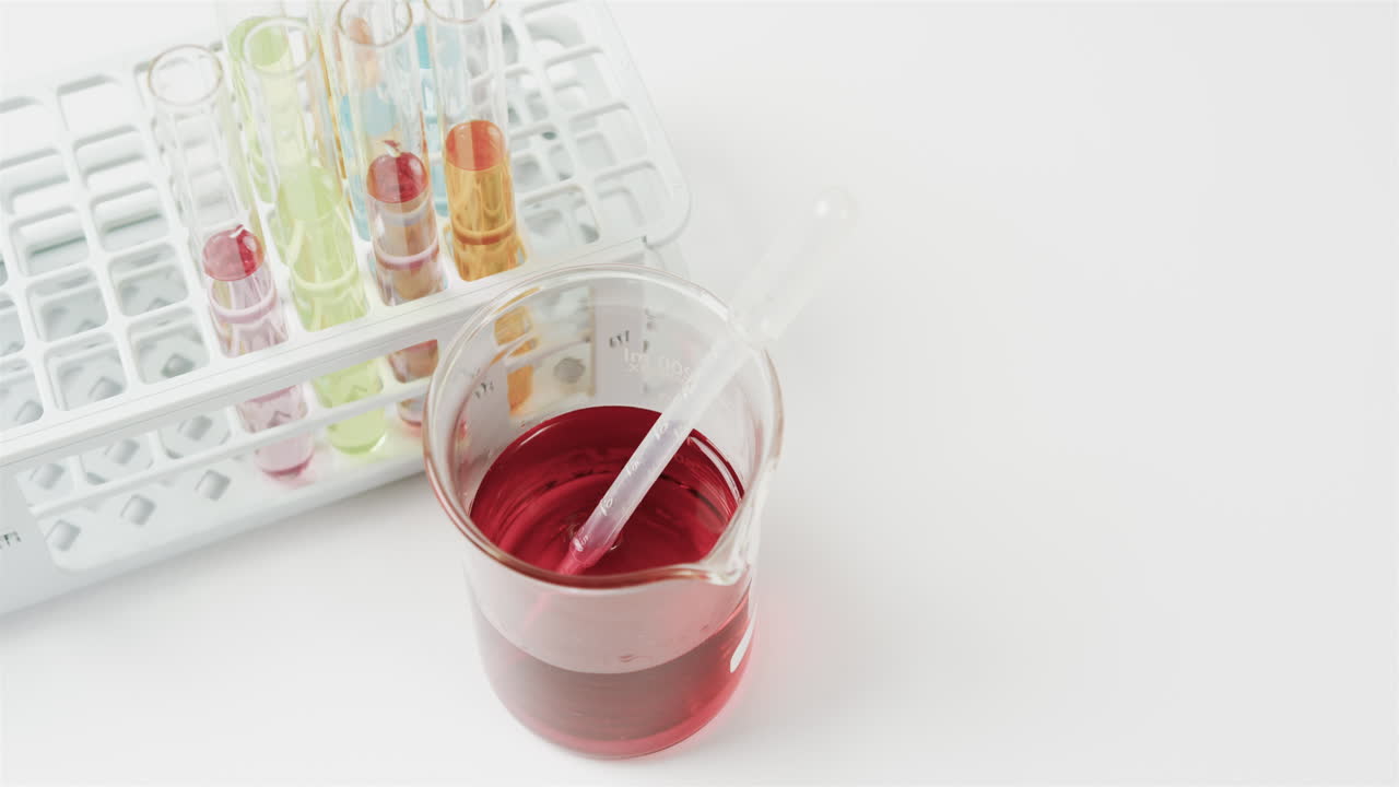 컬러 액체는 백색 배경에 시험 튜브가 서서히 움직이는 컵에 담겨 있습니다.