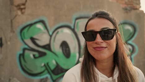 joven modelo de moda con gafas de sol posa para la cámara y se acerca mientras sonríe a la cámara