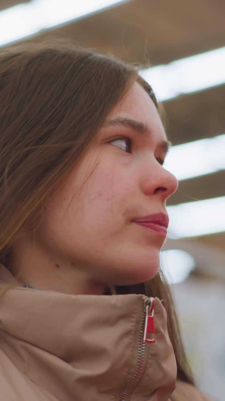 primer plano de una joven con una chaqueta marrón, mirando a su alrededor en un centro comercial. el fondo está borroso, enfatizando su expresión curiosa y observadora