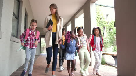 teacher walking with diverse group of students in school hallway, smiling together