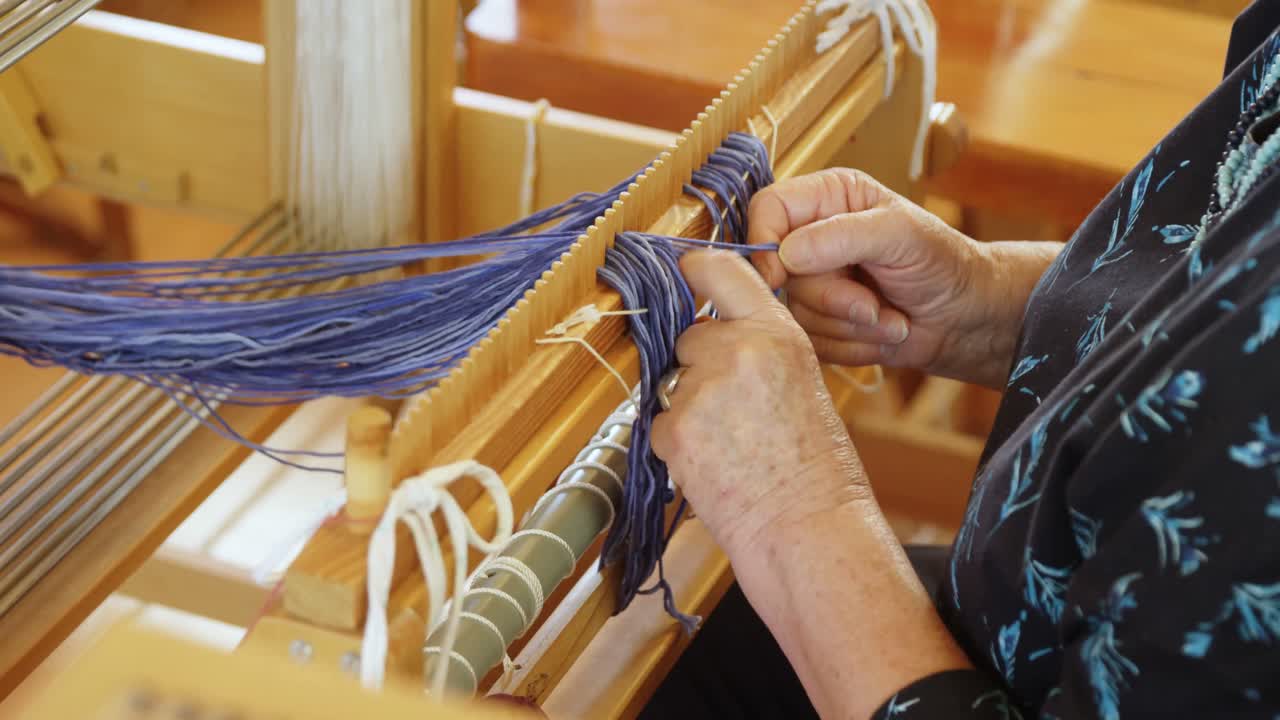 sección media de una anciana mujer caucásica preparando y sentada en una máquina de telar a mano en el taller 4k