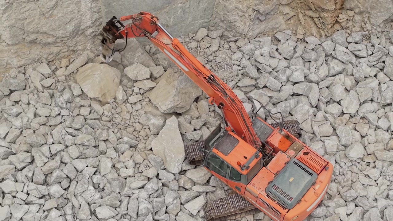 Excavator with hydraulic breaker crushing quarry rocks