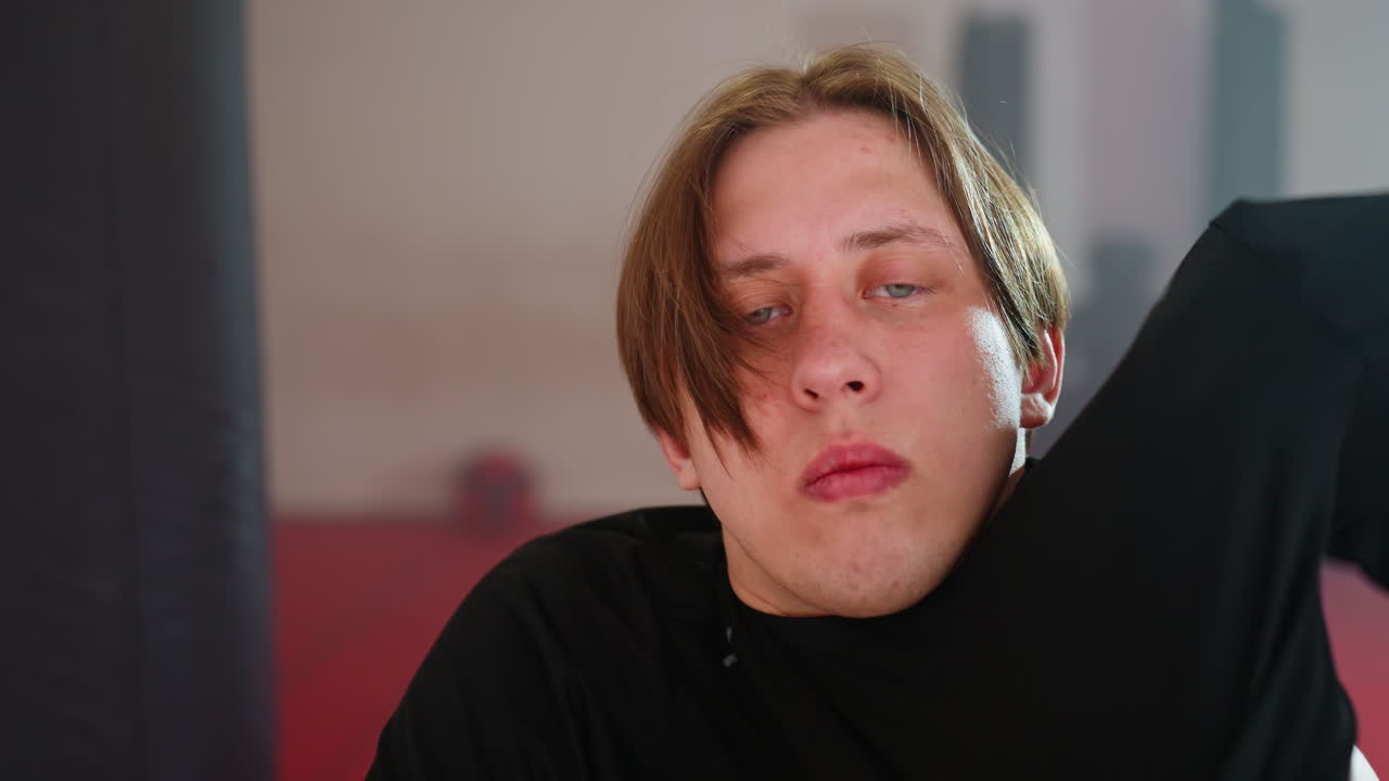 Guy grips black shirt near waist while preparing to change clothes, showing midsection and hands holding fabric in focused motion inside gym environment with red floor, fitness,transition