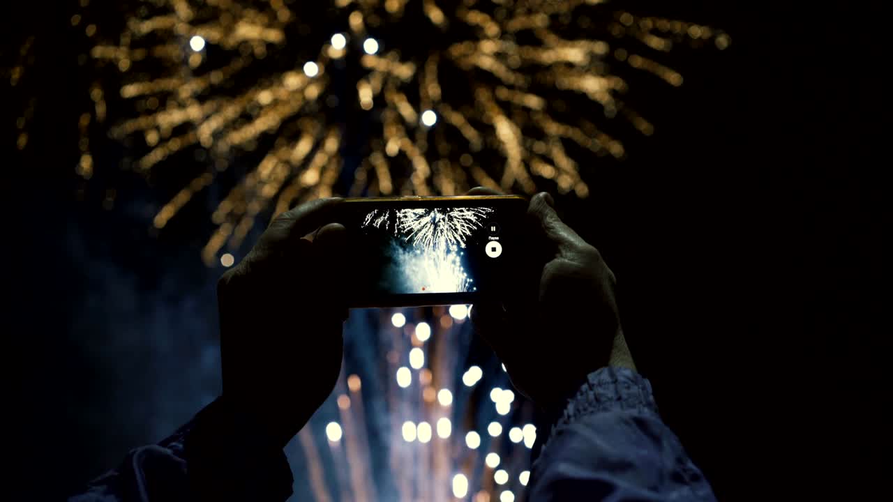 Silhouette di un uomo che fotografa fuochi d'artificio nel cielo notturno. Bellissimo spettacolo in onore della festa.