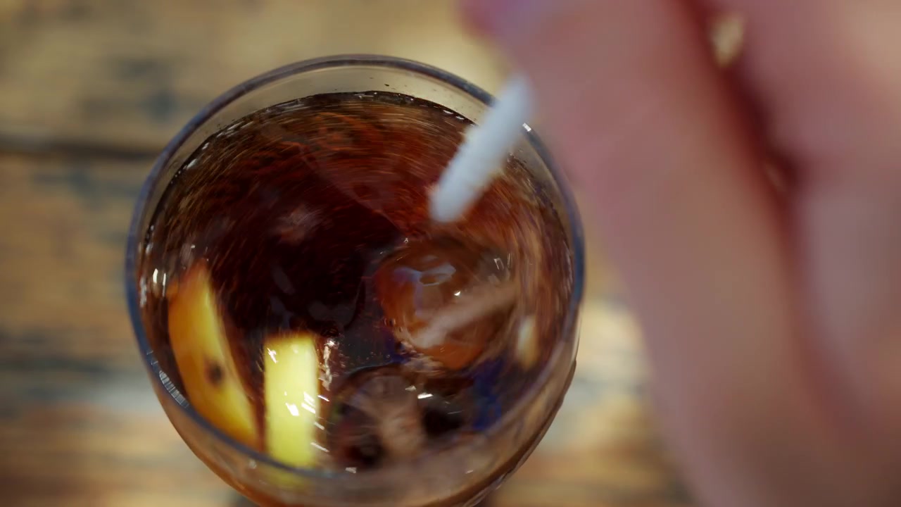 Primo piano di una bevanda cola ghiacciata con fette di limone mescolata con una cannuccia bianca in un bicchiere trasparente.