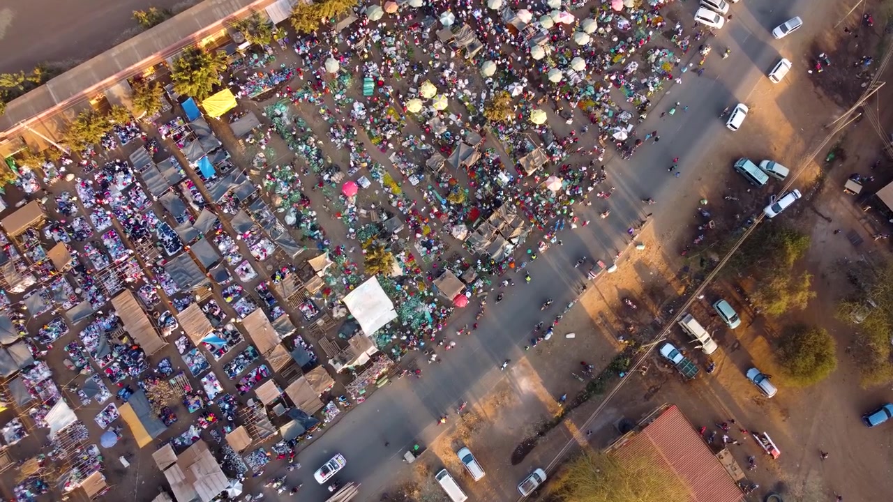 Ohromující letecký pohled na africký otevřený trh s barevnými deštníky, přeplněnými stánky a místními lidmi obchodujícími s čerstvými produkty pod teplým sluncem v Keni.
