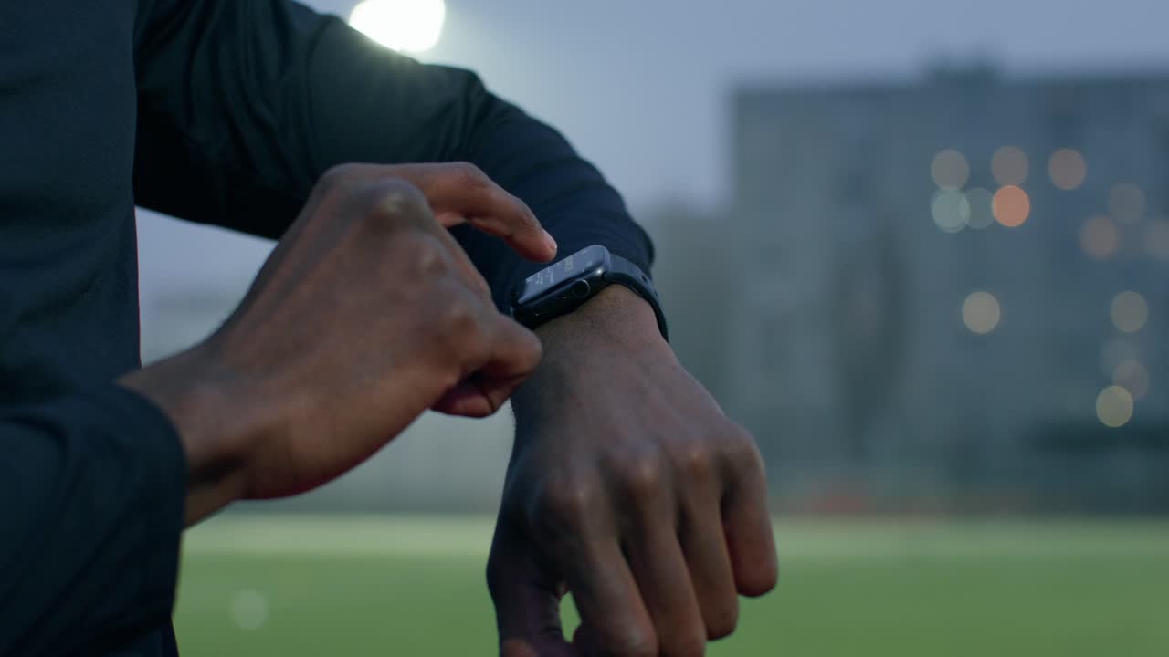 Athlete checking smartwatch at night on a sports field