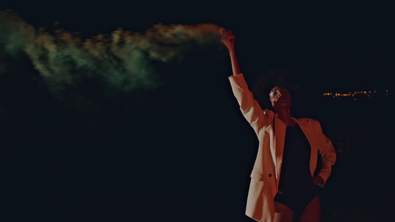 Model using colorful grenade at night zoom on. Trendy sexy woman looking camera