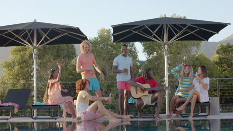 happy diverse friends with drinks talking and dancing in the sun at pool party, slow motion