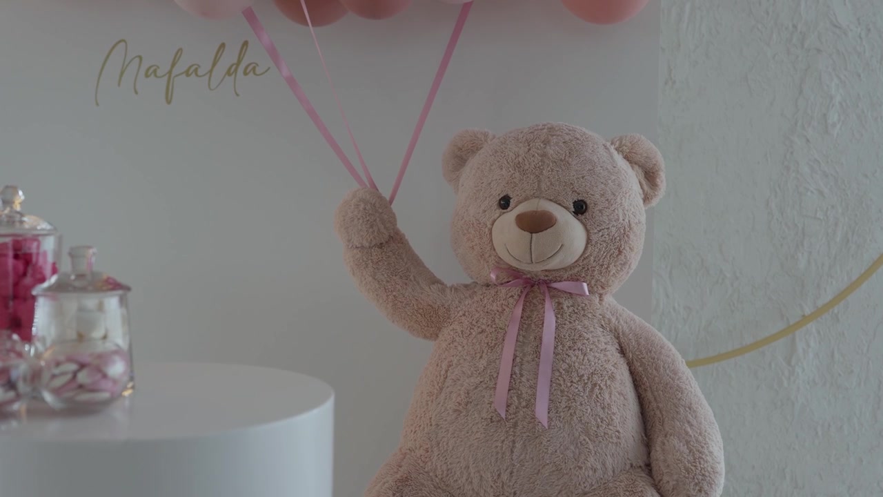 Beige plys-bamse med lyserøde balloner og slikglas ved en babyfest for en pige.