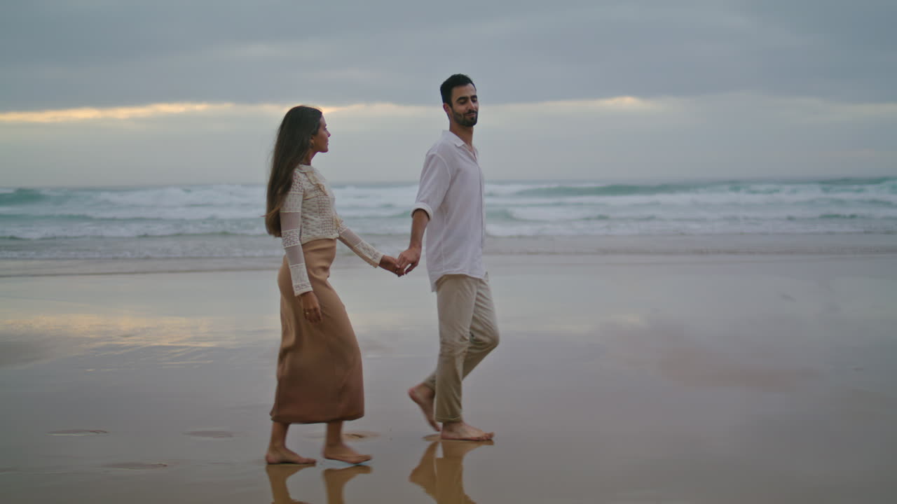Young spouses relaxing beach at evening. Happy lovers walking sea shore vertical