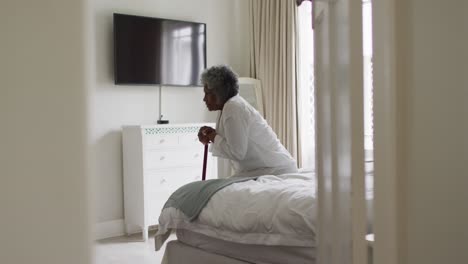 senior african american woman holding walking stick sitting on the bed at home