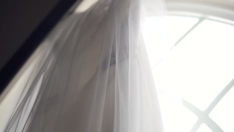 side angle shot of a beautiful wedding dress hanging from a large church window sill - slow motion left to right pan