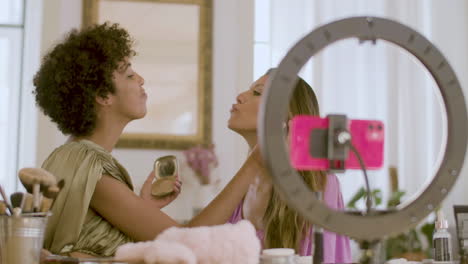 young black woman doing make-up on her female friend and sending kisses to the camera