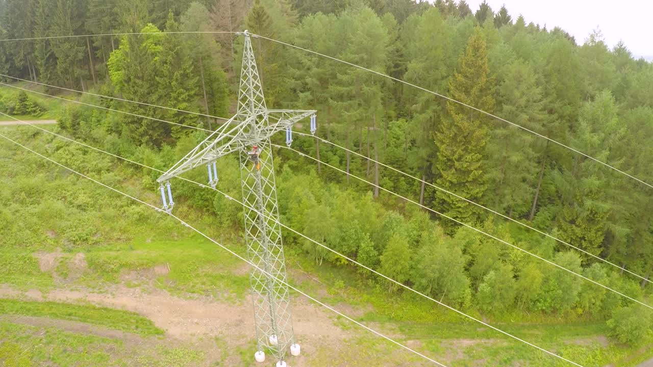 A worker on an electricity pylon in a dense green forest, maintaining power lines, aerial view