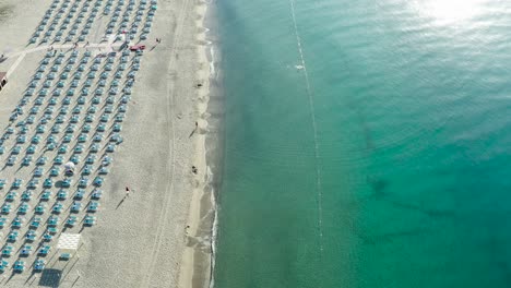 Luftaufnahme-Des-Schönen-Meeres-Und-Des-Strandes-Mit-Sonnenschirm-Am-Sonnigen-Tag,-Seelandschaft-Und-Hügelberg-Auf-Backgrond,-Simeri-Mare,-Kalabrien,-Süditalien