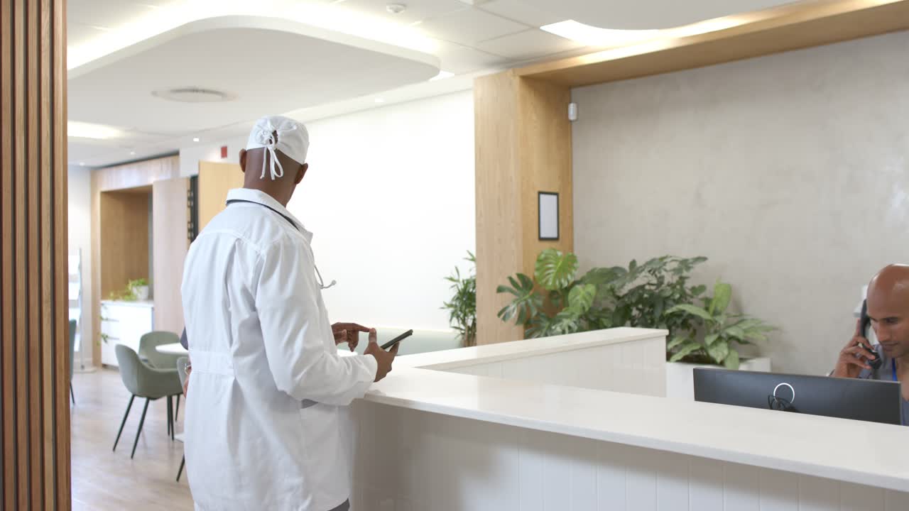 Clinico afroamericano si dirige verso la reception della clinica con uno stetoscopio, tenendo un tablet ed esaminando la cartella clinica