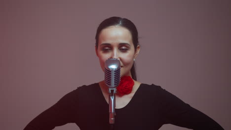 a focused female singer stands confidently in front of a vintage microphone with her hands on her waist. her determined expression and elegant black attire