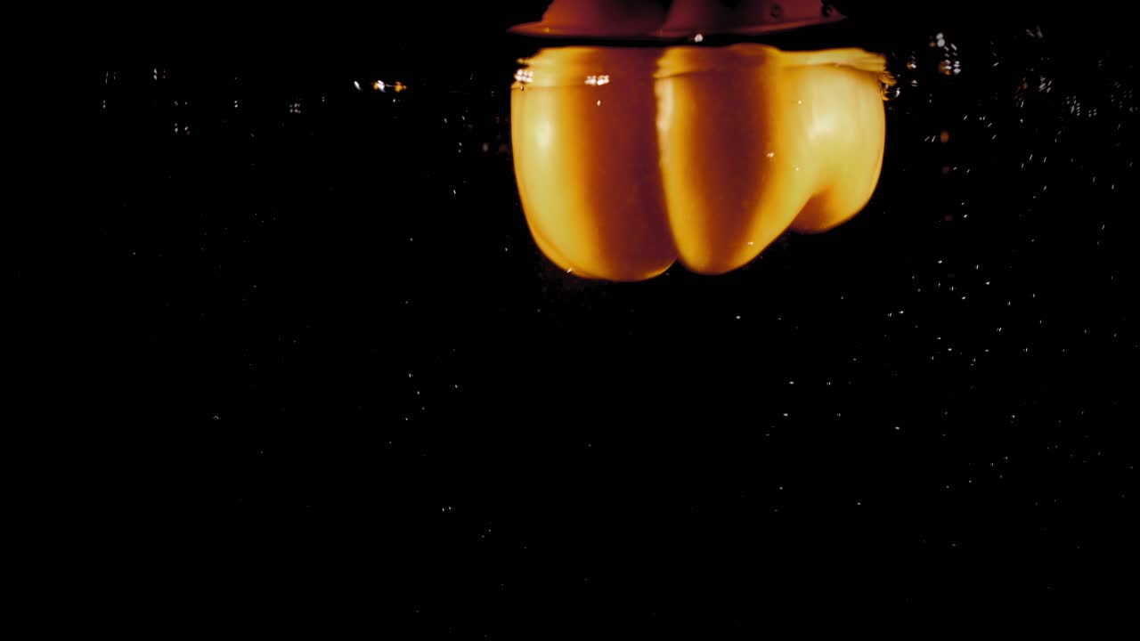 pimentón amarillo cayendo al agua con burbujas sobre fondo negro