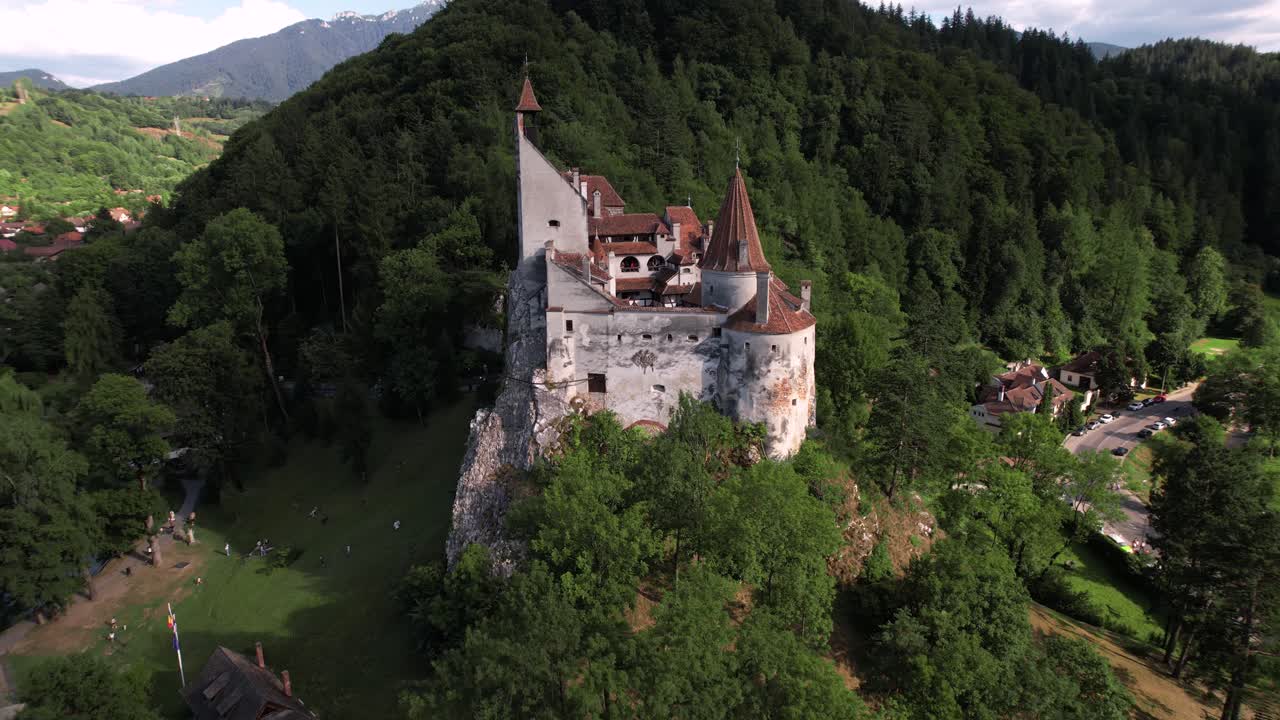 Dramatic drone shot slowly orbiting around Bran Castle. Medieval architecture surrounded by the green hills and forests of Transylvania.