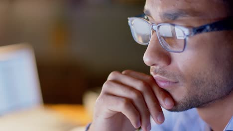 focused biracial businessman wearing glasses at desk using computer in office at night, slow motion