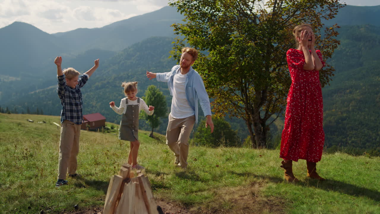 familia activa jugando bailando en la colina verde. padre alegre saltando con los niños
