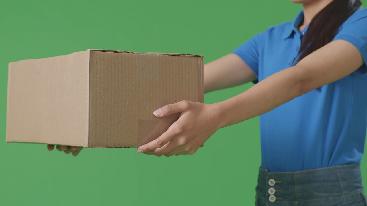 close up de un mensajero femenino en uniforme azul dando un cartón a alguien mientras lo entrega en el fondo de la pantalla verde en el estudio
